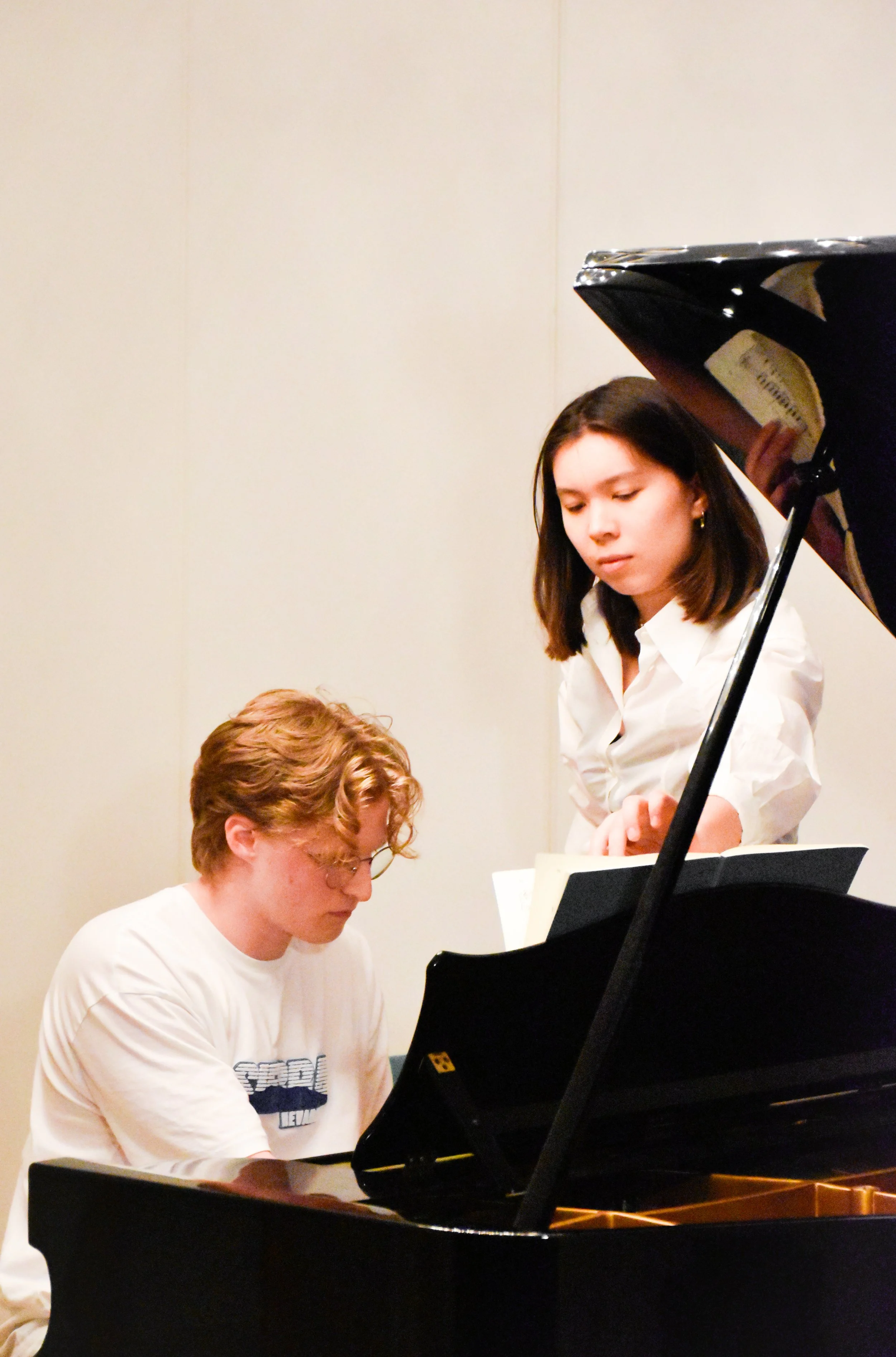 Zwei junge Menschen, ein Mädchen und ein Junge, spielen Klavier in einem Raum, das Mädchen steht und das Mädchen sitzt am Klavier.